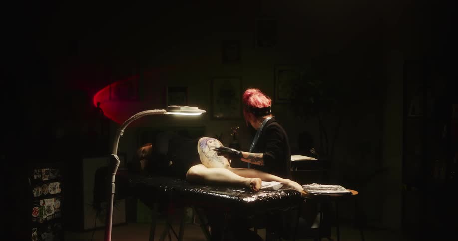 Female tattoo artist drawing a tattoo on a womans upper thigh