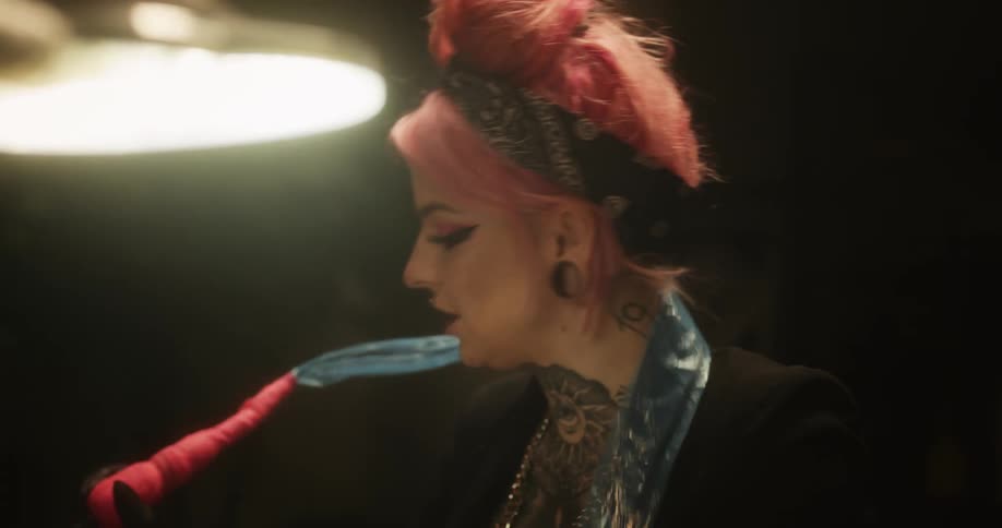 A female tattoo artist with pink air working on a client
