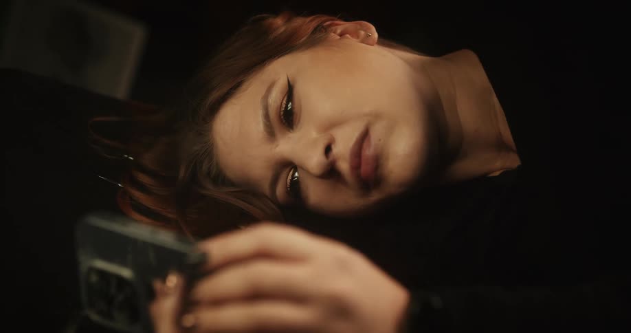 A woman lying down scrolls on her cell phone
