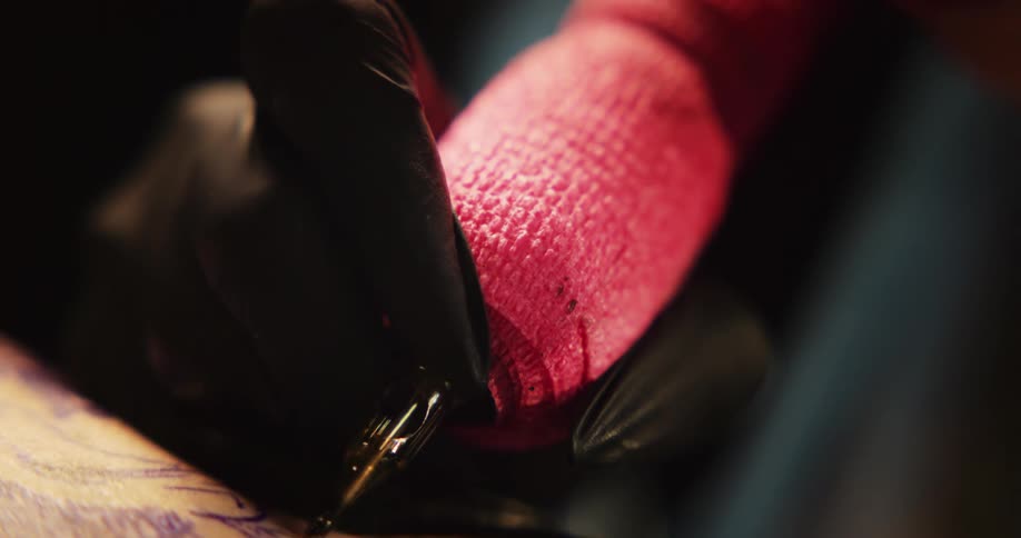 Close up of a tattoo artist with colorful hair working on the skin of a client