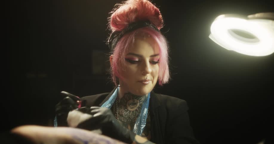 Close up of a tattoo artist with colorful hair working on the skin of a client