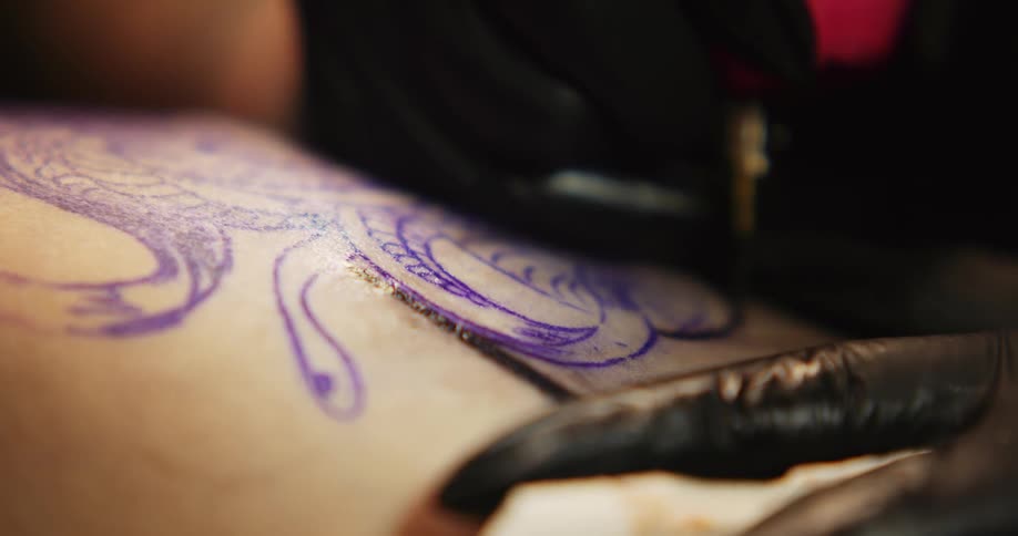 Skin being tattooed with tattoo machine as artist wipes with napkin
