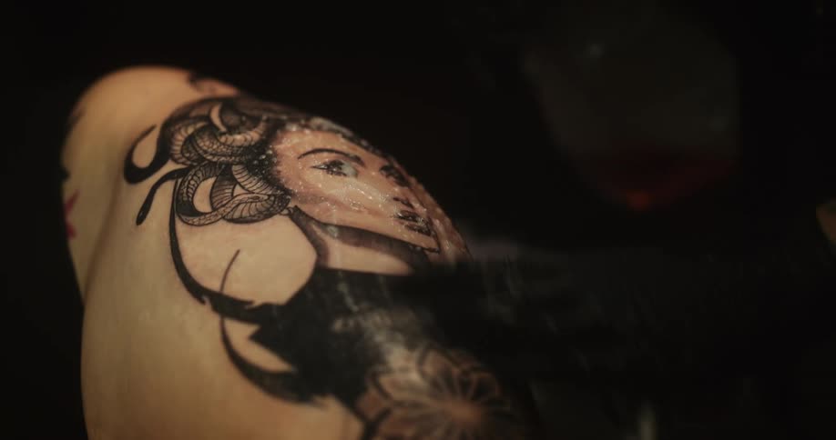 A person wearing black gloves is spraying a solution on a womans tattoo then wiping it off