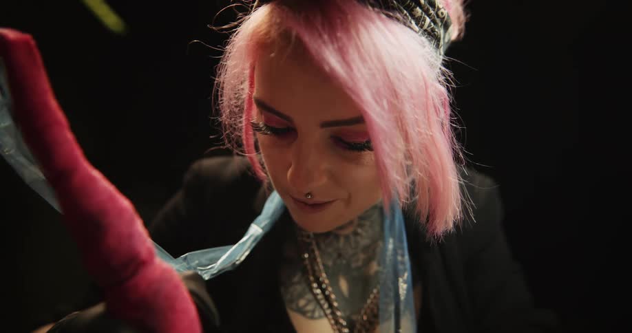 Close up of a tattoo artist with colorful hair working on the skin of a client