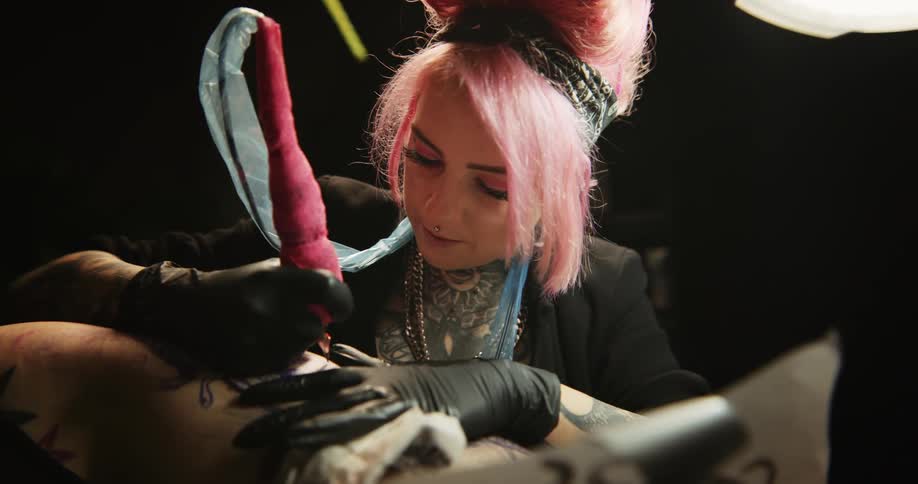Close up of a tattoo artist with colorful hair working on the skin of a client