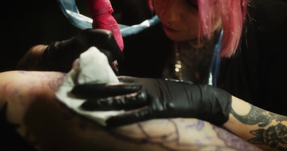 Close up of a tattoo artist with colorful hair working on the skin of a client