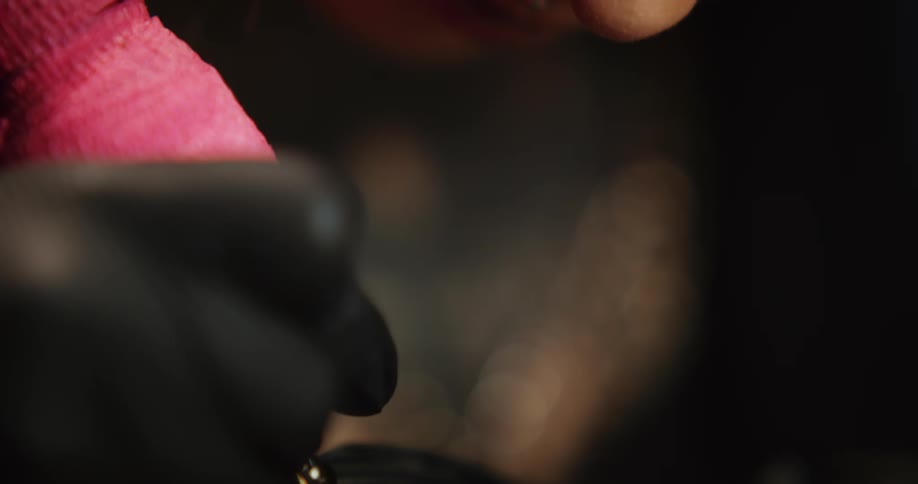 Close up of a tattoo artist with colorful hair working on the skin of a client