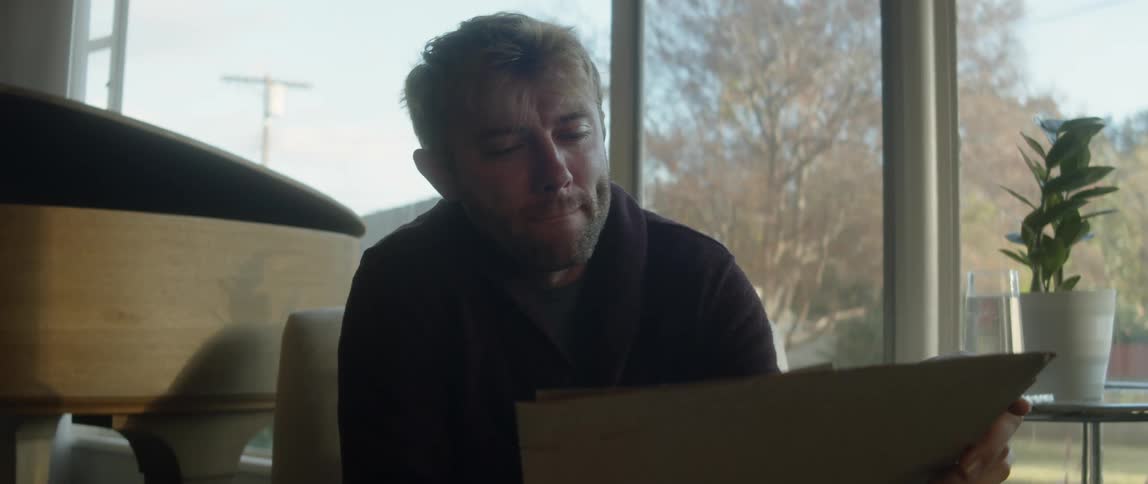 A man is sitting in his living room looking at pictures and he stops to think