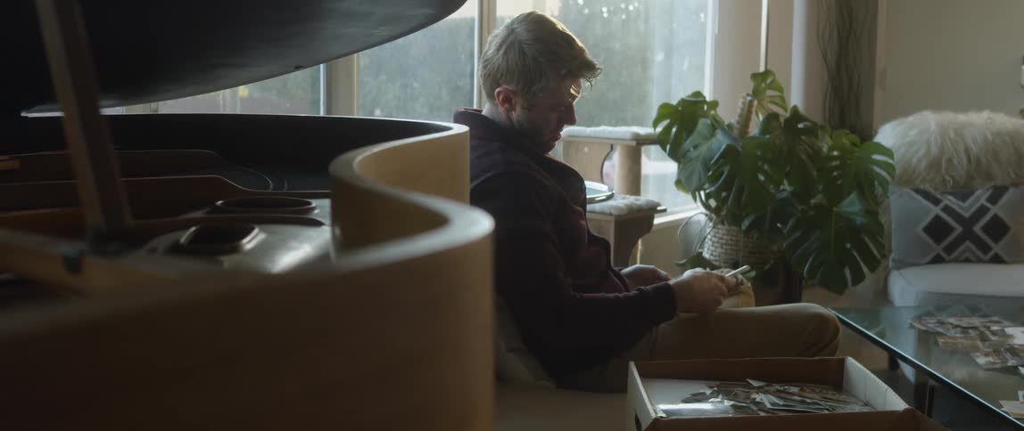 A man is sitting down in his living room looking at a handful of photographs he is holding
