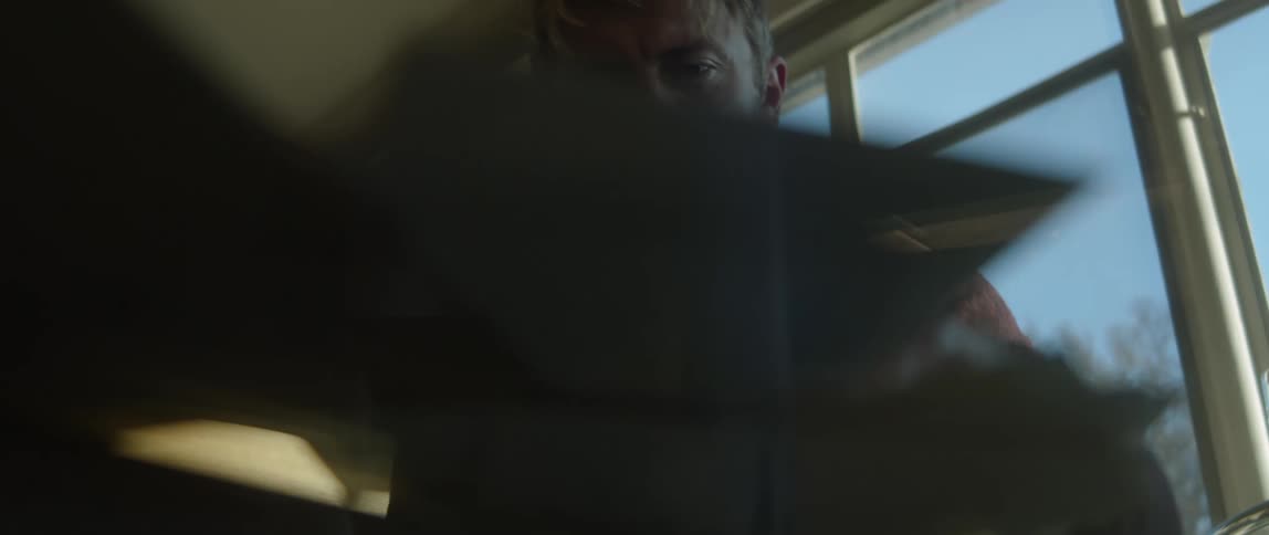 A man is sitting down looking at photographs and he tosses them on a glass table
