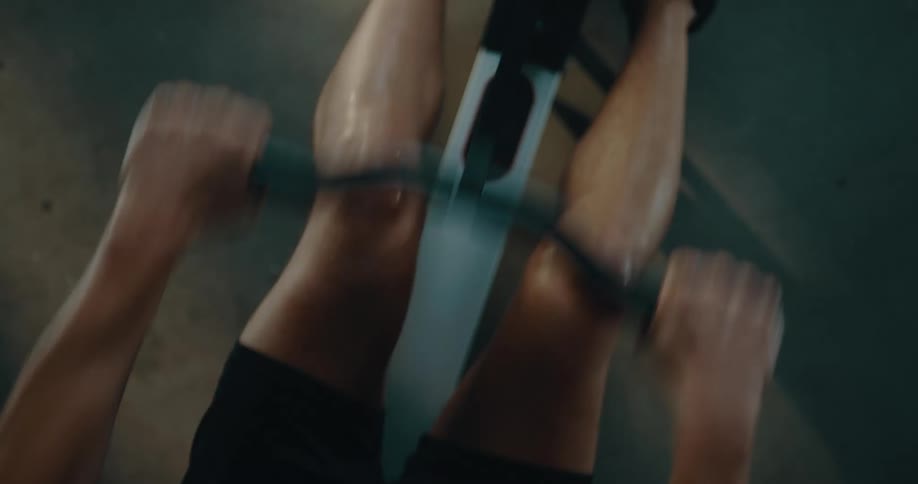 Top down view of a strong muscular man sweating while working out on a rowing machine