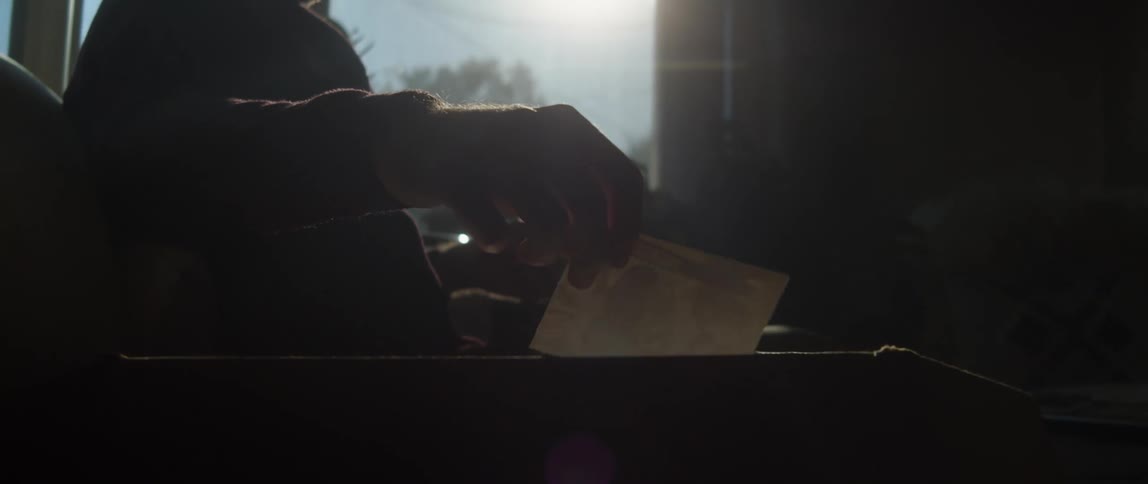 Silhouette of a man handling old photographs found on a cardboard box at home