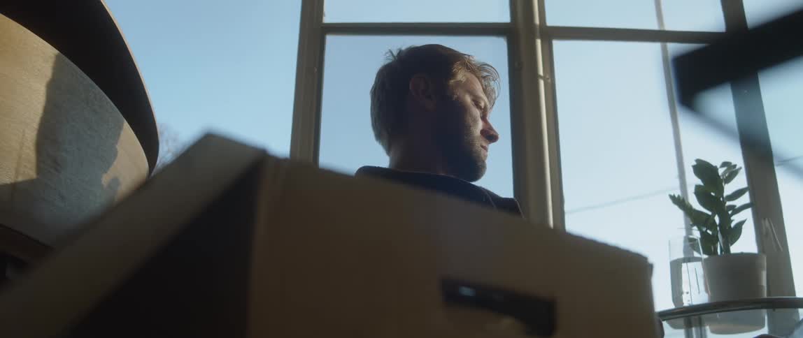 Man sitting behind a cardboad box at home looks out the window
