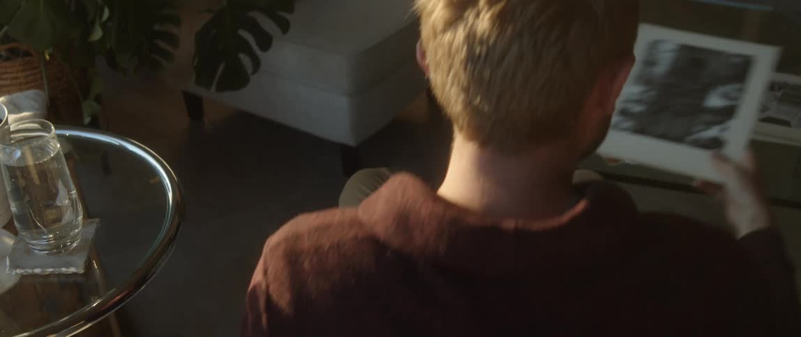 A man is sitting down looking at a photograph he is holding and he sets it on the table