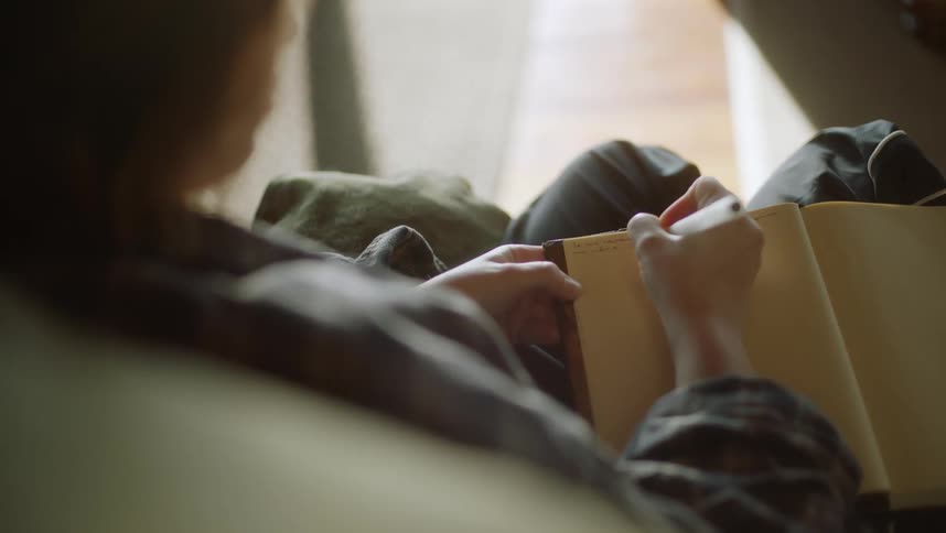 A woman is sitting down writing in a book