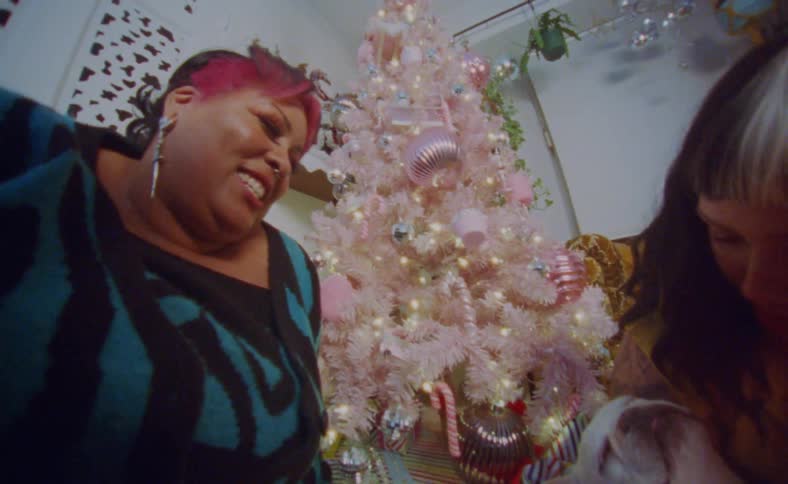 Young happy couple sitting next to a colorful christmas tree playing with their dog