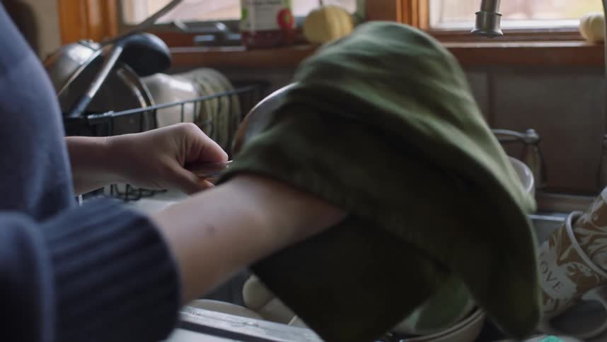 Woman drying pot with green towel near kitchen sink