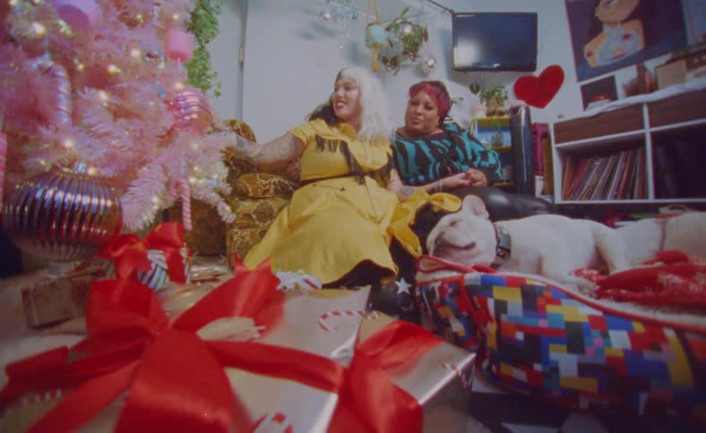 Young happy couple sitting next to a colorful christmas tree with their dog