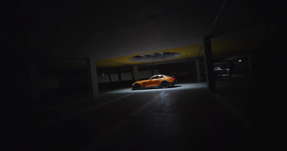 An FPV drone shot of an orange sports car parked in an empty showroom