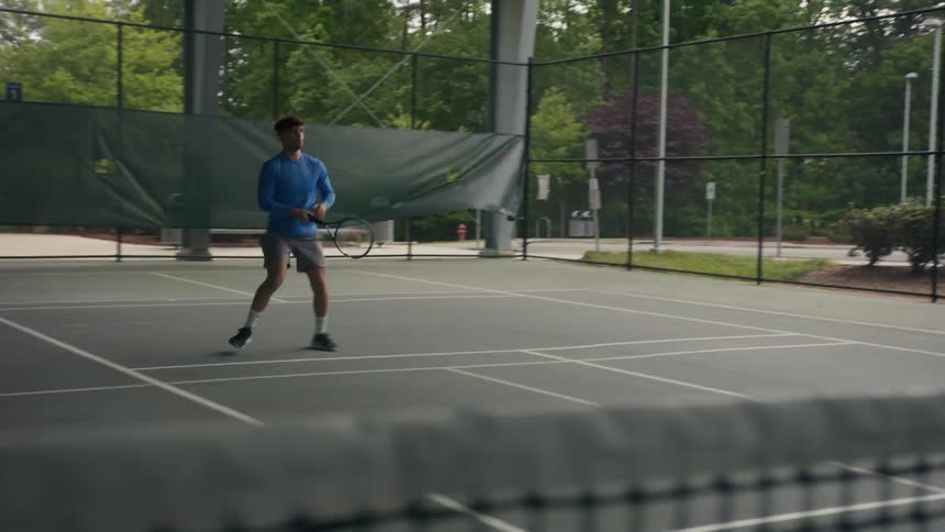 A man is standing on a tennis court holding his racket and standing ready as he moves to hit the ball