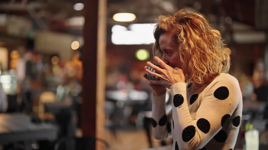 A woman in a restaurant picks up a hot drink and takes a sip