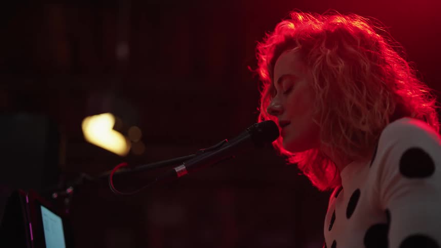 Light shines on a woman as she is singing into a microphone