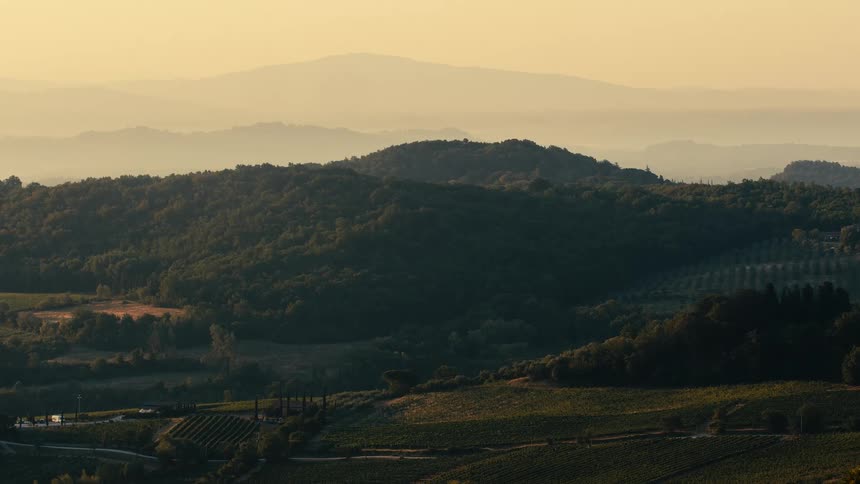 Farmland sits at the foot of a forested mountain under a hazy sky