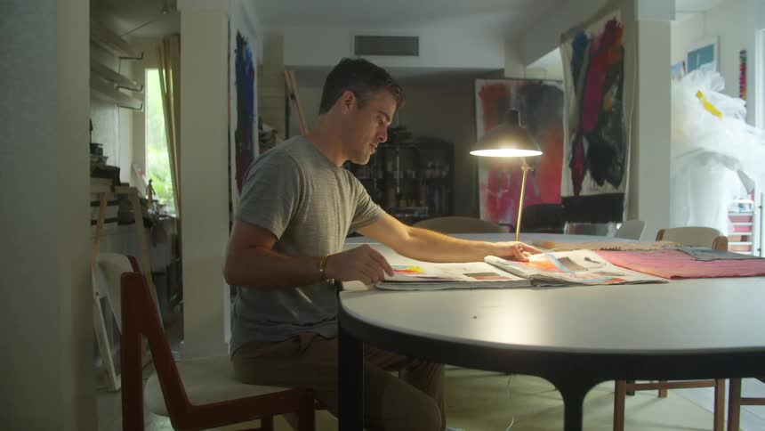A man is sitting down at a table flipping through the pages of a large book with pictures