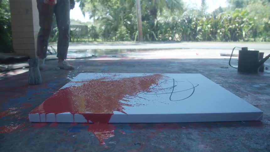 Man splashes paint across canvas lying on the concrete