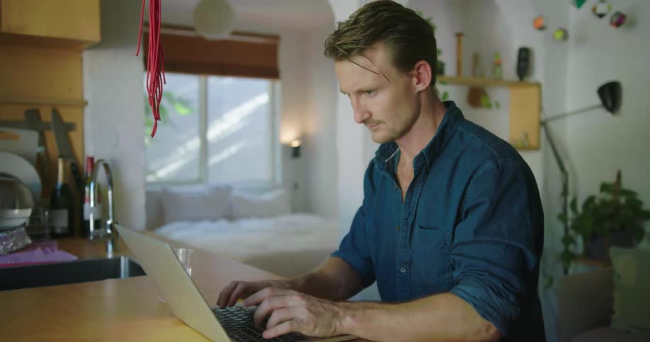 Man types on a laptop at a kitchen counter