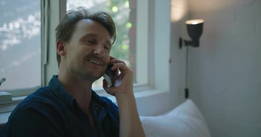 A man sits on with a laptop while talking on the phone