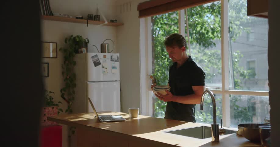A man is eating from a bowl in his kitchen