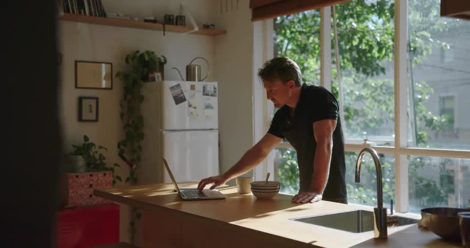 Man standing at a kitchen counter typing on a laptop