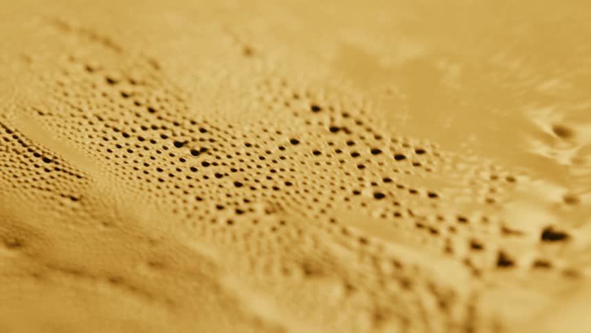 Light shines on a gold organic liquid substance and holes emerge as it ripples and moves and then melts down
