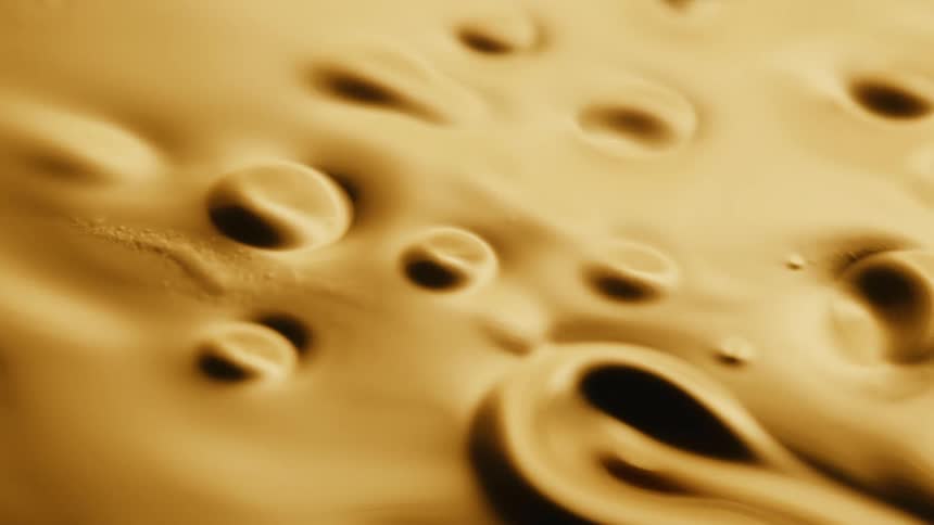 Light shines on a gold organic liquid substance and shapes and holes emerge as it moves