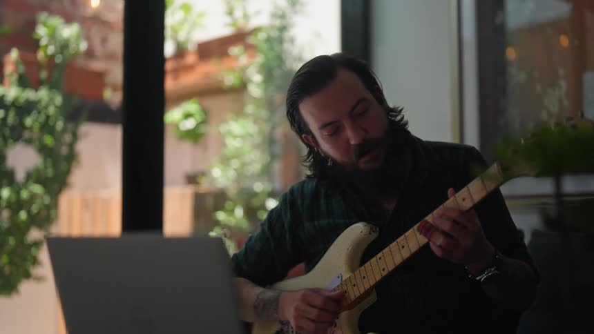 A man is talking on the laptop while playing guitar