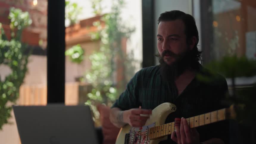 A man is playing the guitar while looking at laptop screen