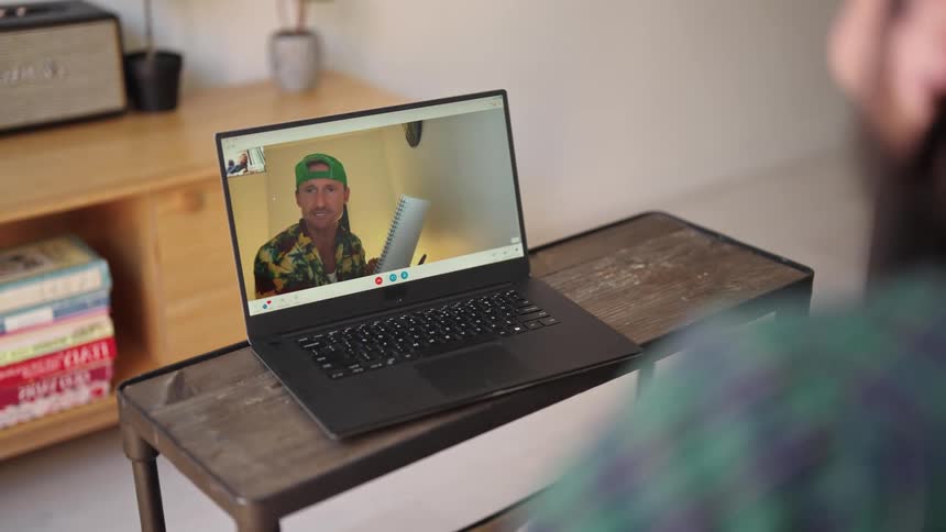 A man sits at home and video chats with his friend on a laptop who is singing