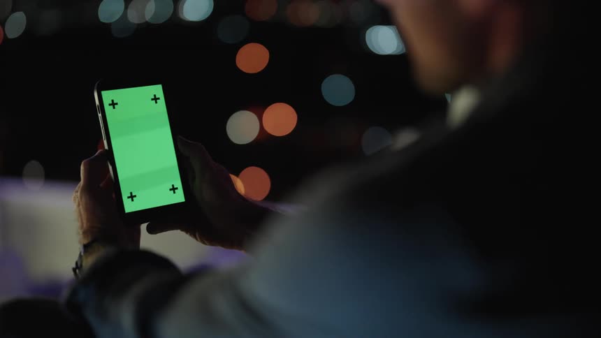 Man wearing shirt texts on smartphone at night outdoors