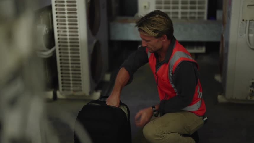 A worker in an orange vest puts his laptop into a backpack and carries them away