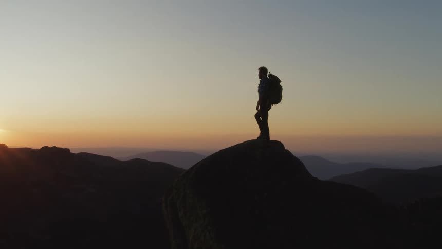 Rear view of man standing on the edge of cliff watching sunset