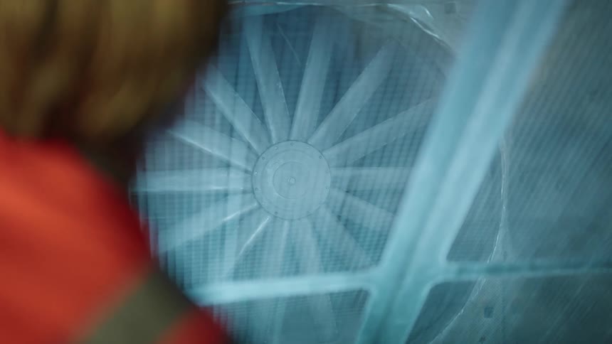 A man is shining a light towards the industrial fan