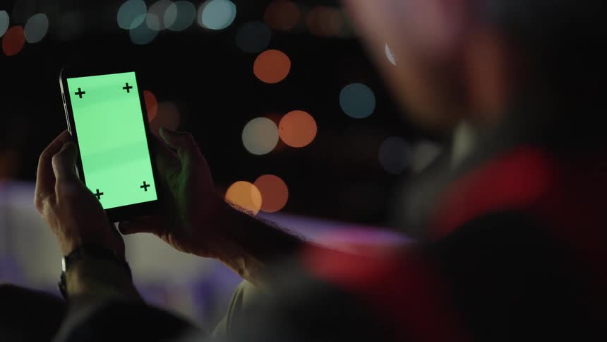 A man is typing on his phone with green screen displayed