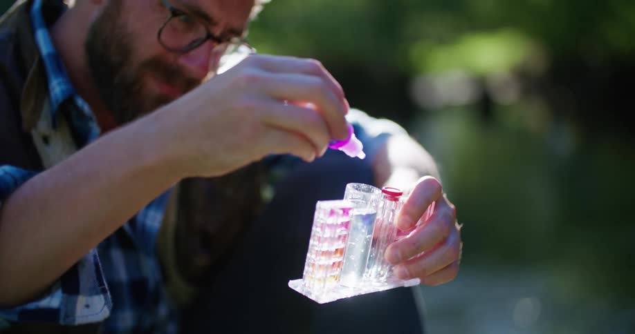 Man sitting on riverbank tests water sample