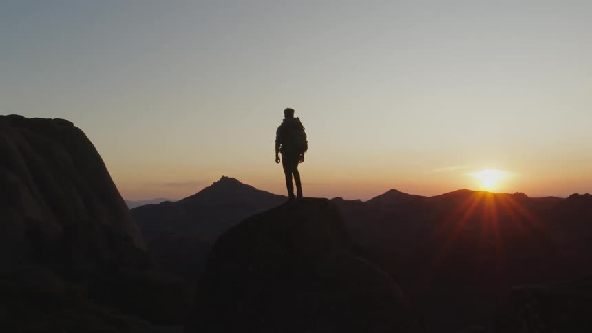 A man out hiking stands on a mountain and watches the sun rise
