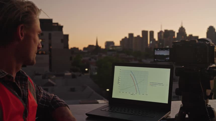 A male hits the record button on a camera that is next to a computer outside