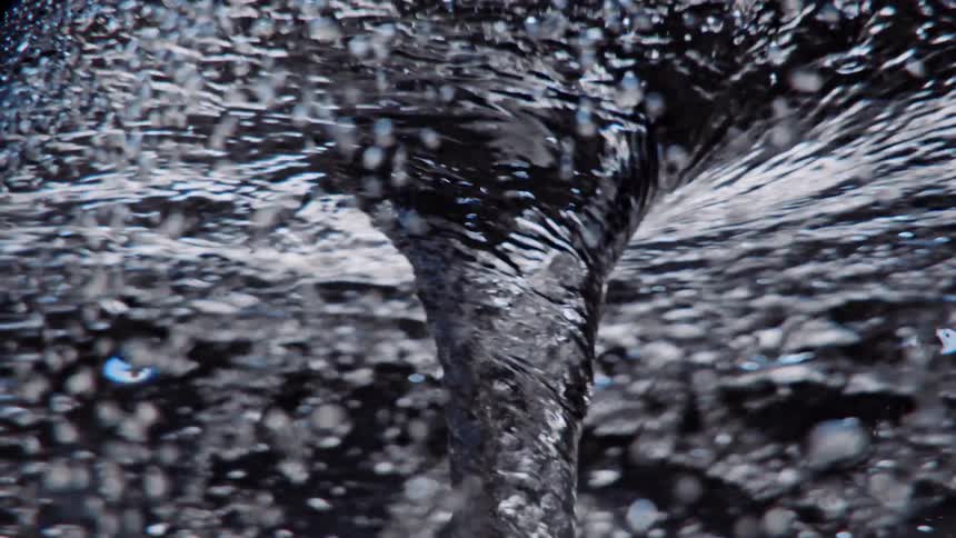 Light reflects on bubbles as they rotate around a swirling water vortex as it twists and turns