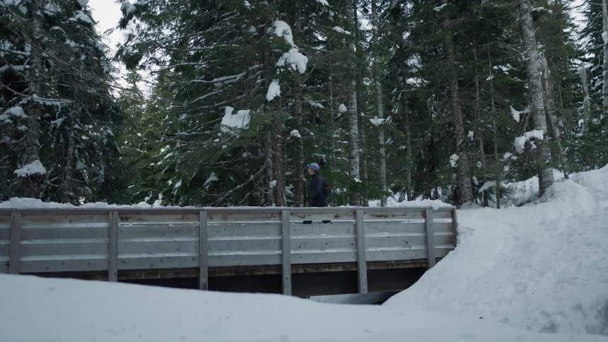 Woman walks over a wooden bridge in a snowy forest