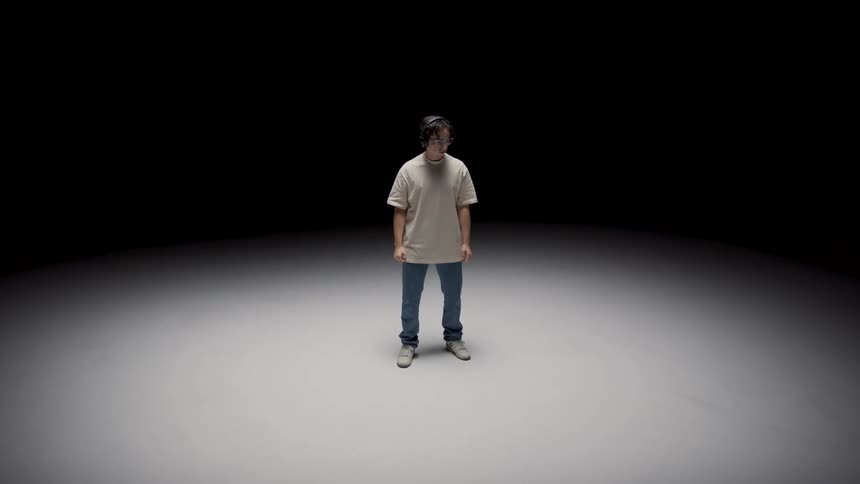 Young man standing in the middle of an empty stage under a spotlight puts on headphones