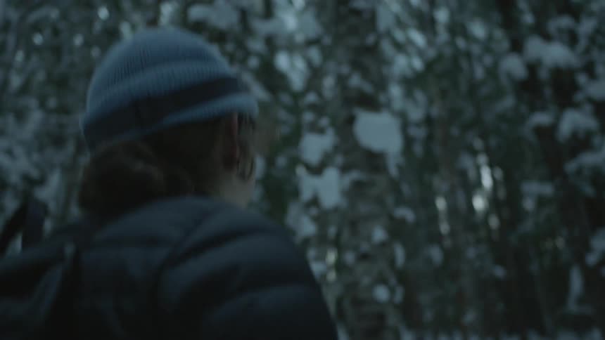 Woman wearing a backpack and beanie walking through a snow covered forest